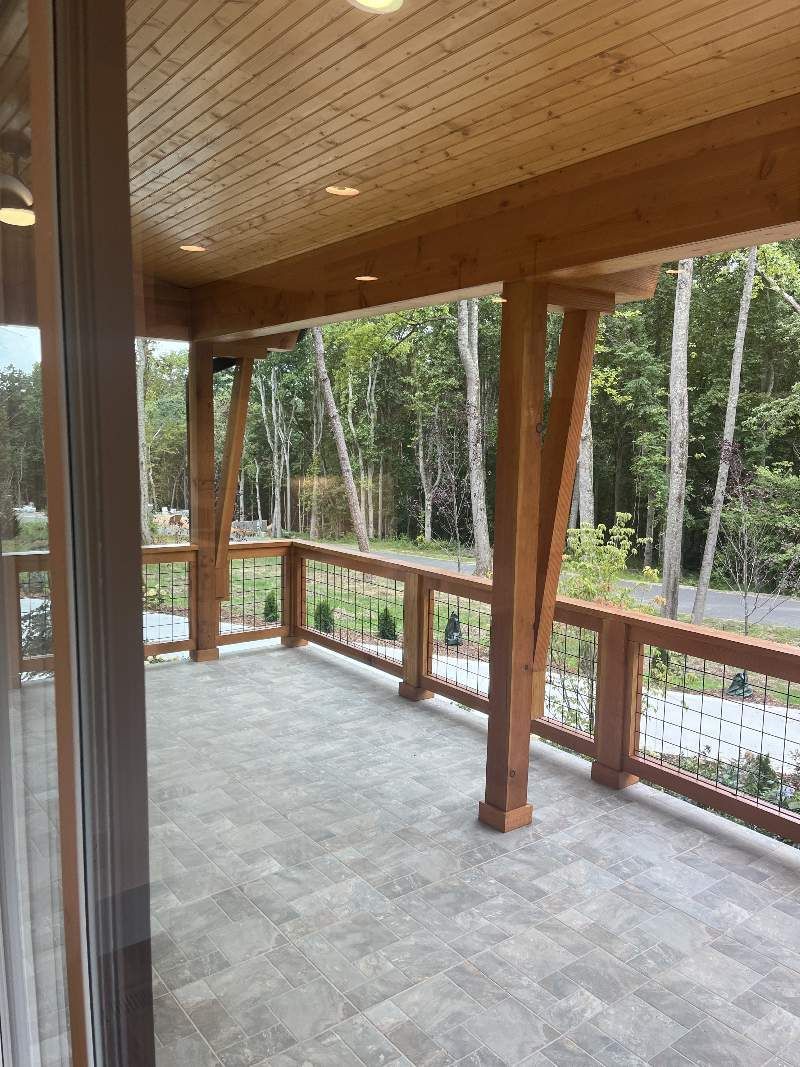 A large porch with a wooden railing and trees in the background.