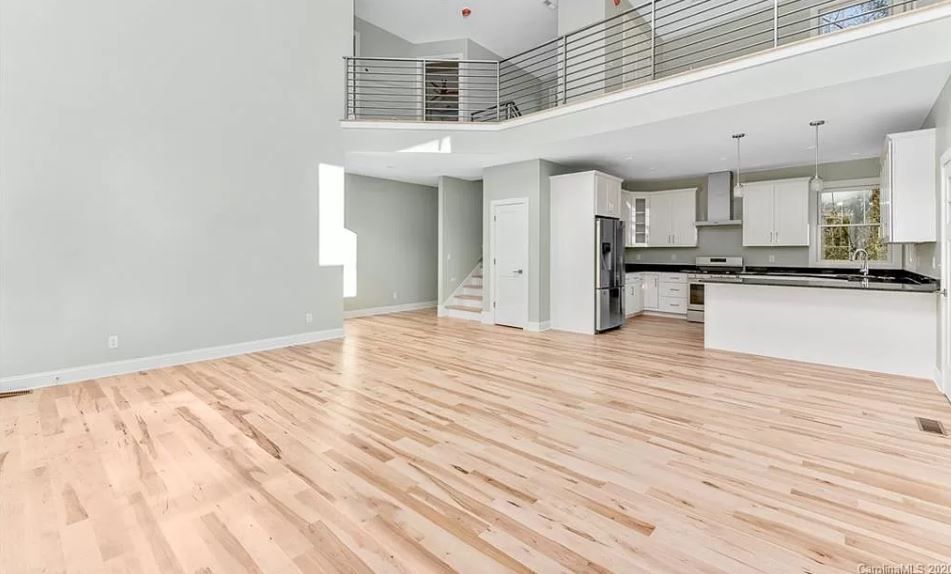 An empty living room with hardwood floors and a kitchen.