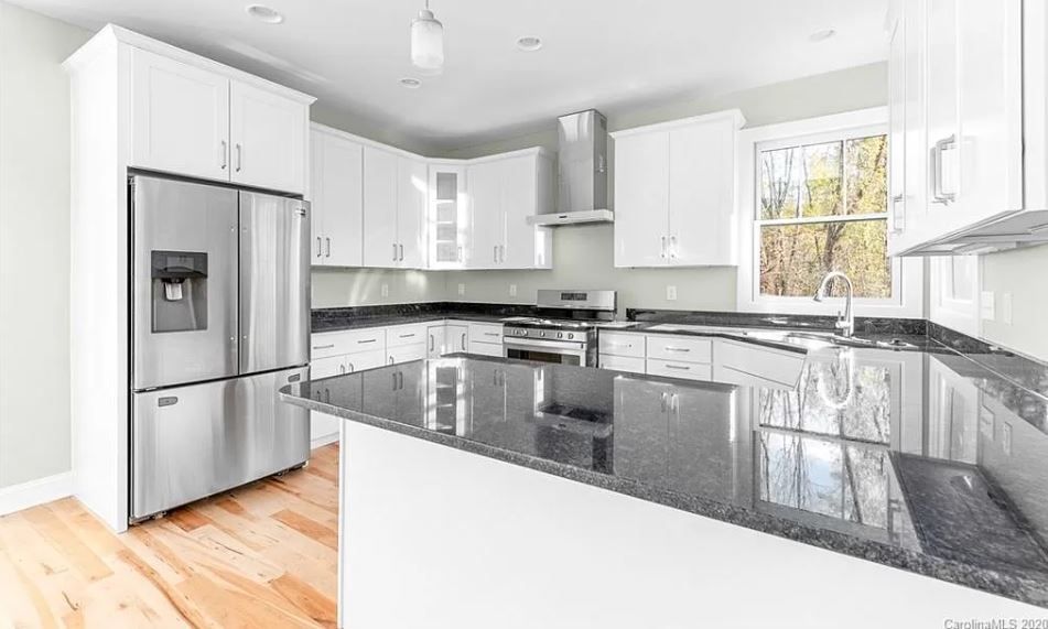 A kitchen with white cabinets, stainless steel appliances, granite counter tops and a refrigerator.