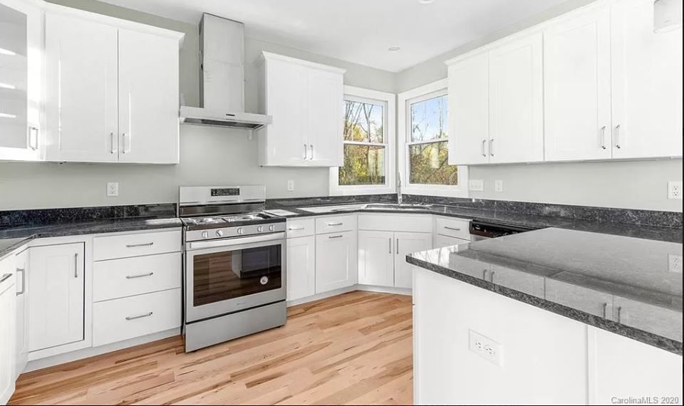 A kitchen with white cabinets, stainless steel appliances, granite counter tops and hardwood floors.