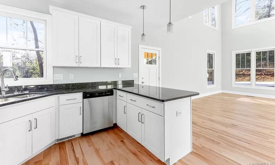 An empty kitchen with white cabinets and hardwood floors.
