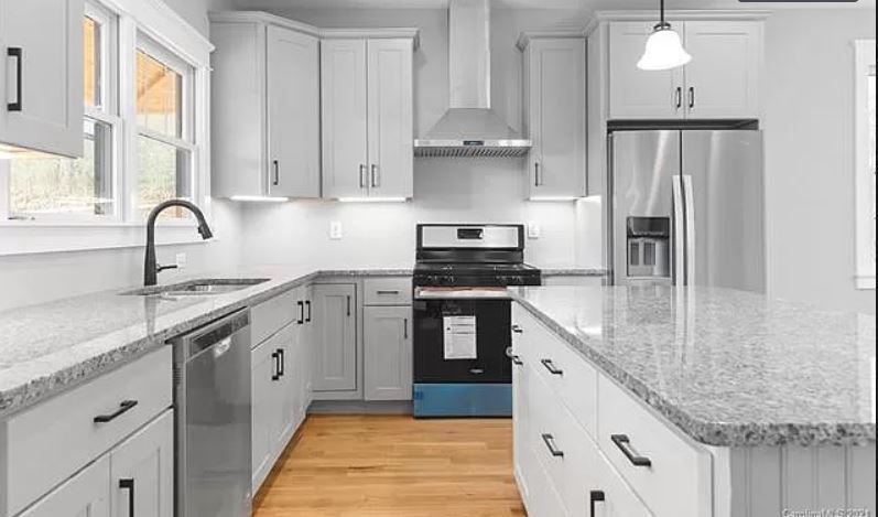 A kitchen with white cabinets, granite counter tops, stainless steel appliances and a large island.