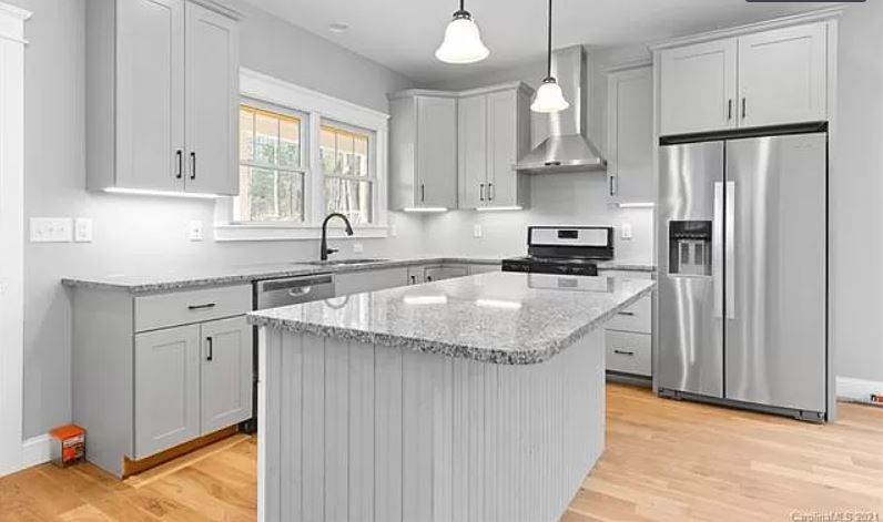 A kitchen with white cabinets, granite counter tops, stainless steel appliances and a large island.