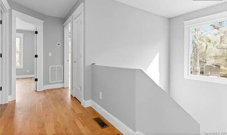 An empty hallway with hardwood floors and a window in a house.