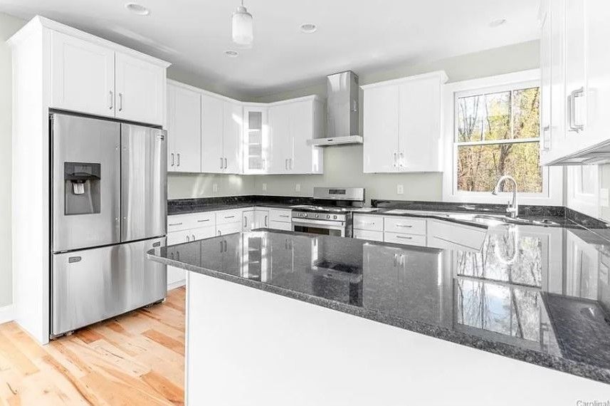 A kitchen with white cabinets, stainless steel appliances, granite counter tops and a refrigerator.
