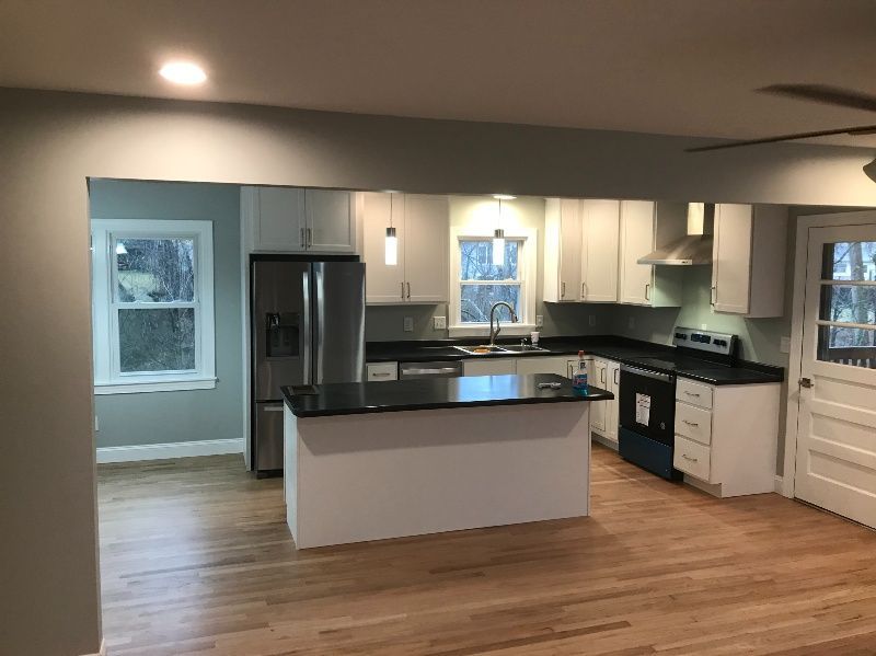 A kitchen with white cabinets, black counter tops, stainless steel appliances and a large island.