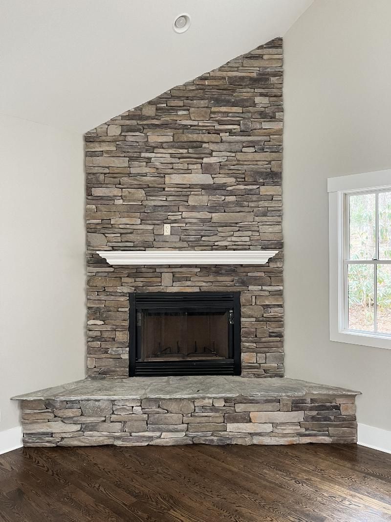A living room with a stone fireplace and a window.
