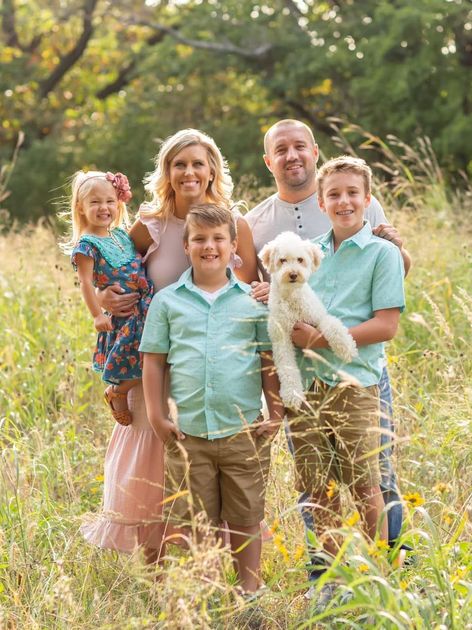 A family is posing for a picture in a field with their dog.