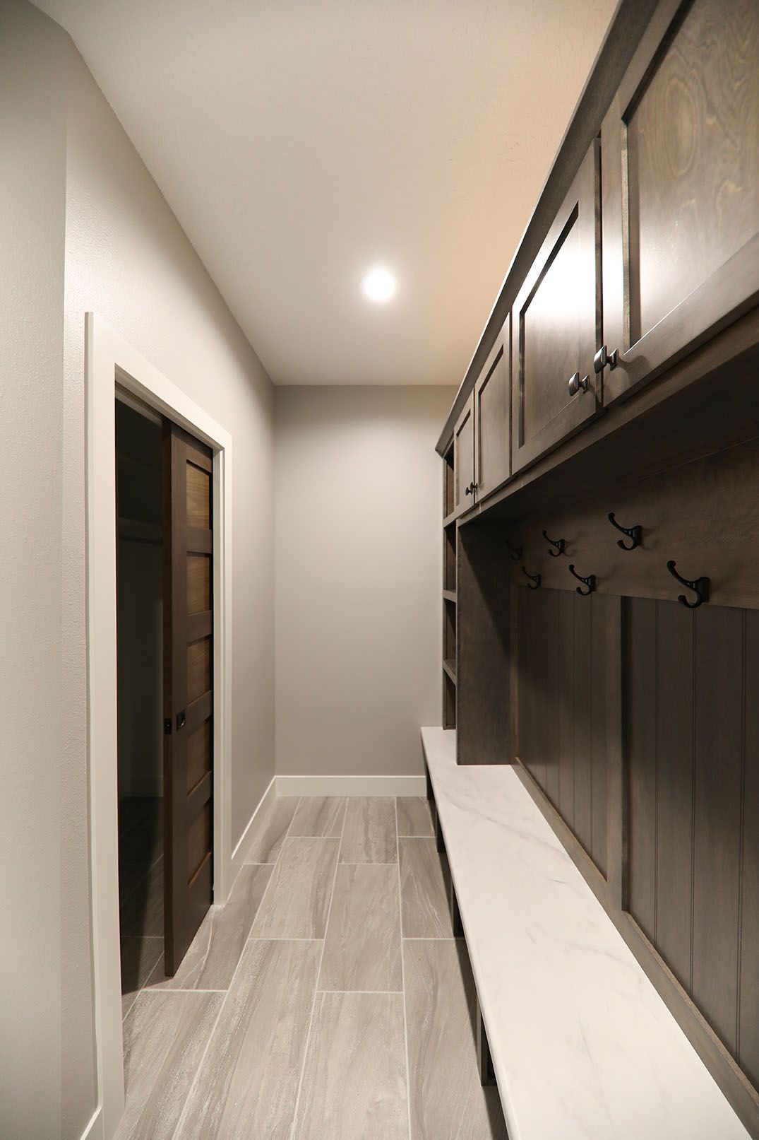 A hallway with a bench , cabinets and hooks on the wall.