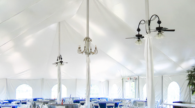 a large white tent with tables and chairs and ceiling fans .