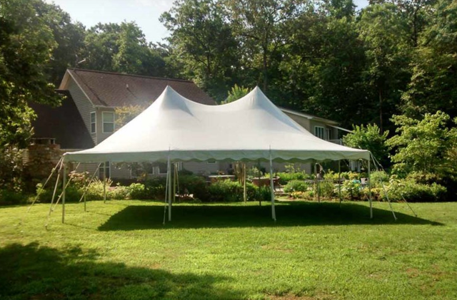 a large white tent is sitting in the grass in front of a house .