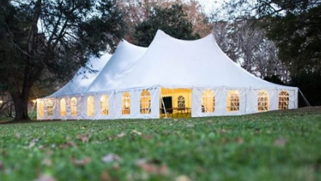 a large white tent is sitting in the middle of a grassy field .