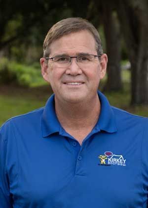 Man in glasses, blue polo shirt with logo, smiling outdoors.