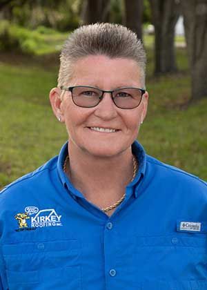 Woman wearing glasses and blue shirt smiles outdoors.