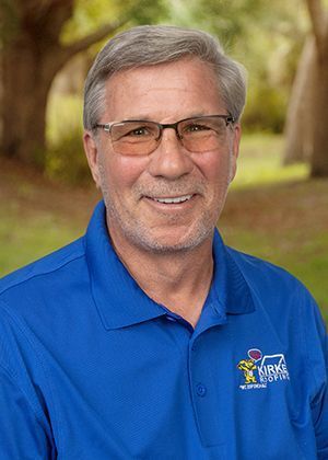 Man wearing glasses and blue shirt with logo, smiling outdoors.