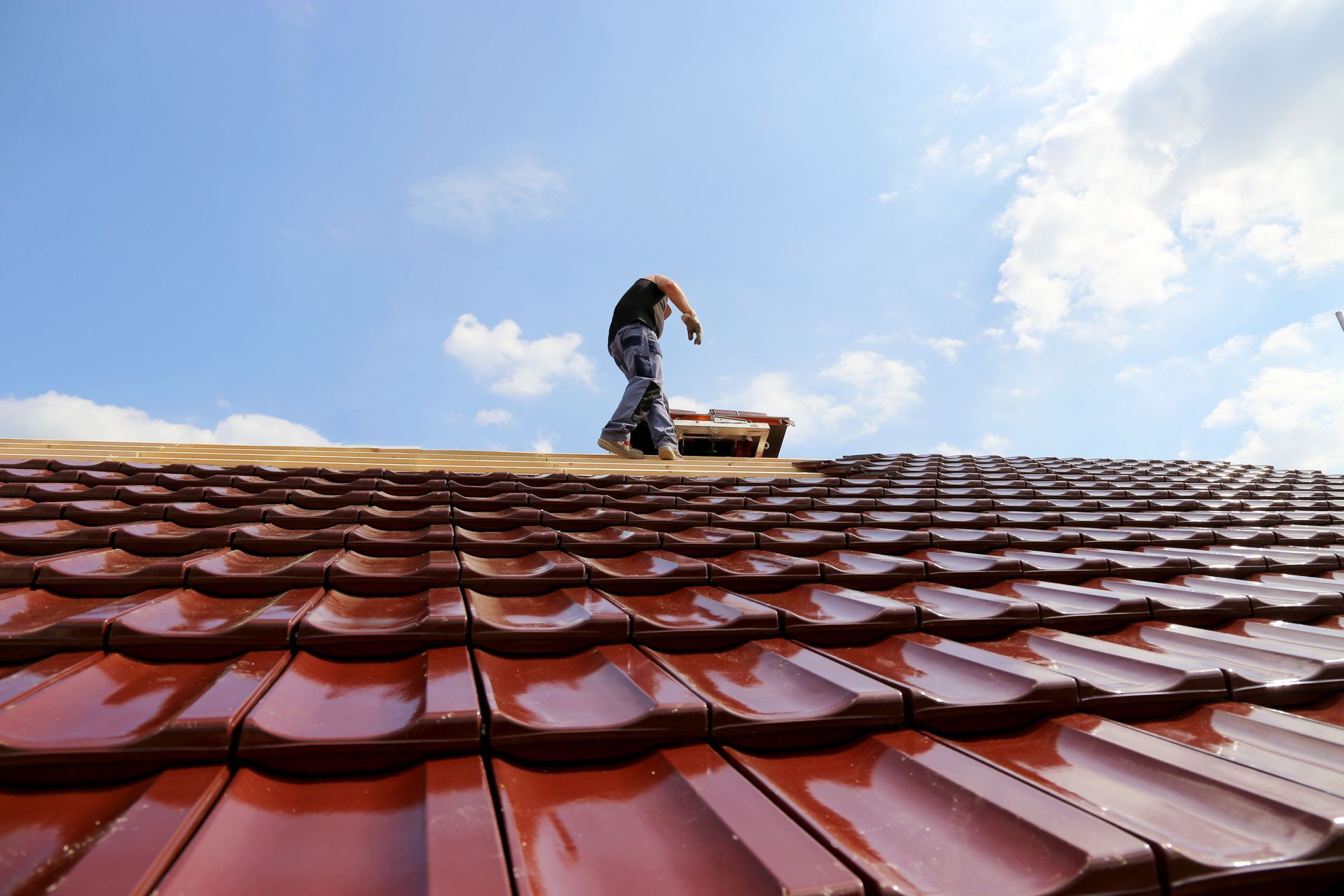 Man on roof with red tiles, blue sky overhead.