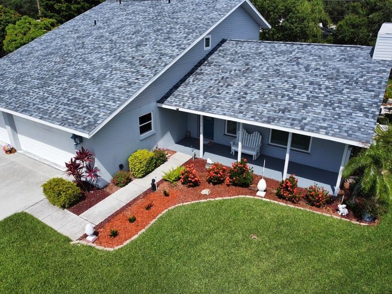 Blue house with gray roof, green lawn, and landscaped flower beds.