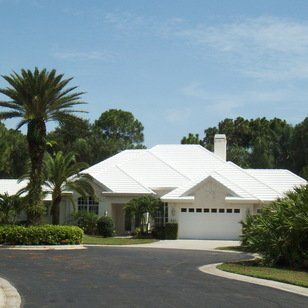 White-roofed house with driveway and palm trees against a blue sky.