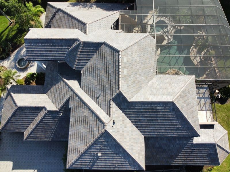 Overhead view of a multi-sectioned house with gray shingle roof. A screened enclosure is visible.