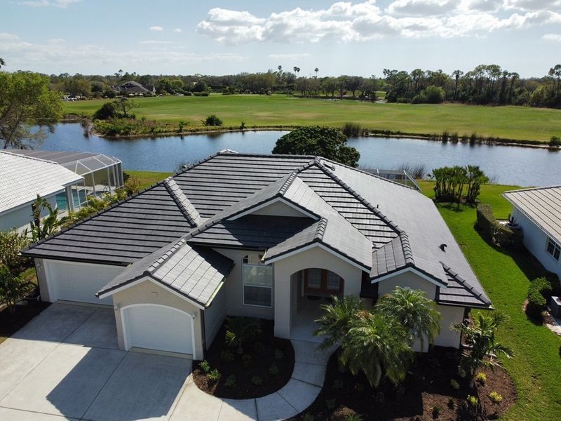 A gray-roofed house overlooking a lake and golf course on a sunny day.