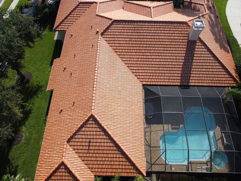 Aerial view of a home with a terracotta-tiled roof and a screened-in pool. Green lawn surrounds the house.