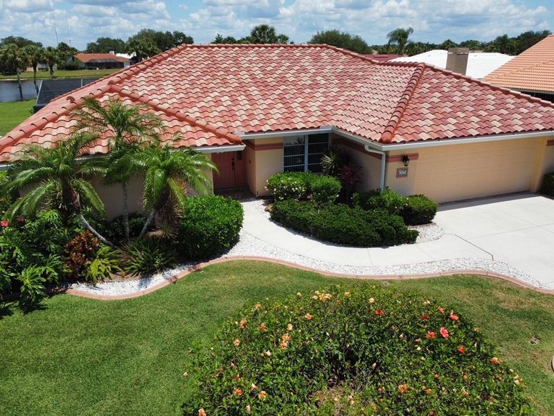 House with red tile roof, beige exterior, green lawn, driveway, and landscaping.