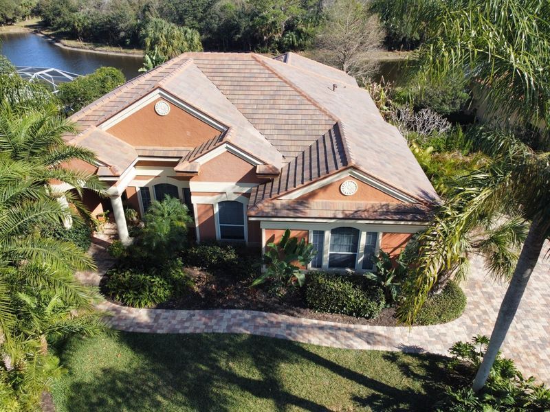 House with terracotta roof, brick walkway, lush green landscaping, and water in the background.