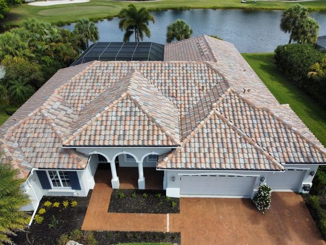 Aerial view of a light-colored house with a terracotta tile roof, overlooking a golf course and water.