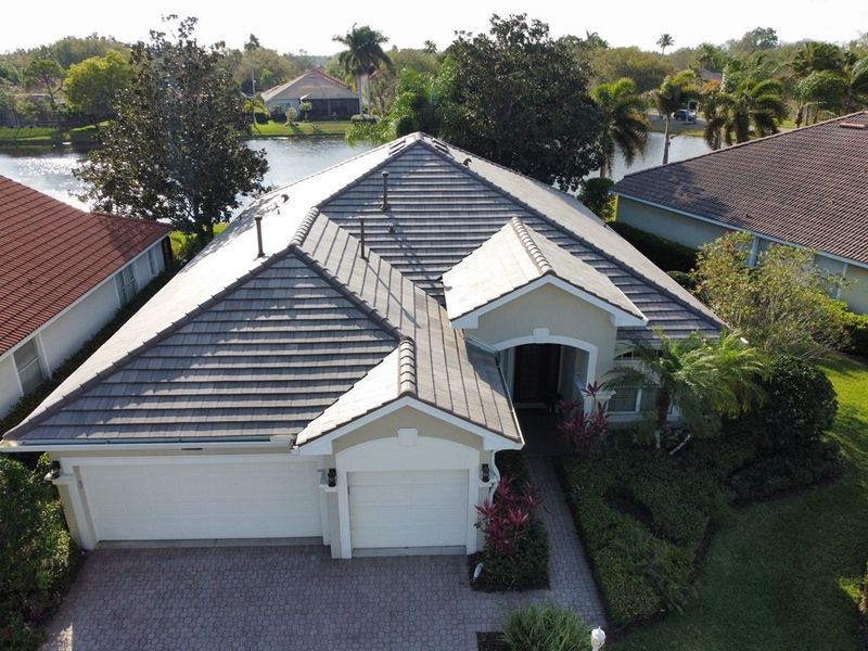 Aerial view of a single-story house with a gray tile roof near a lake and other houses.