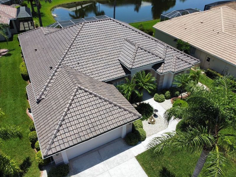 Aerial view of a house with brown tile roof, surrounded by green grass, near a pond.