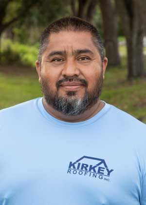 Man wearing light blue Kirkey Roofing shirt smiles outdoors.