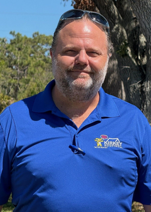 Man with sunglasses on his head, wearing a blue polo shirt with a logo, outside.