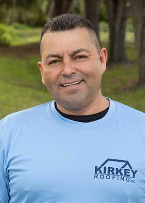 Man in light blue shirt with Kirkey Roofing logo smiling outdoors.