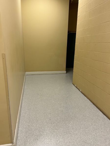Narrow hallway with light gray floor and beige walls leading to a dark opening.