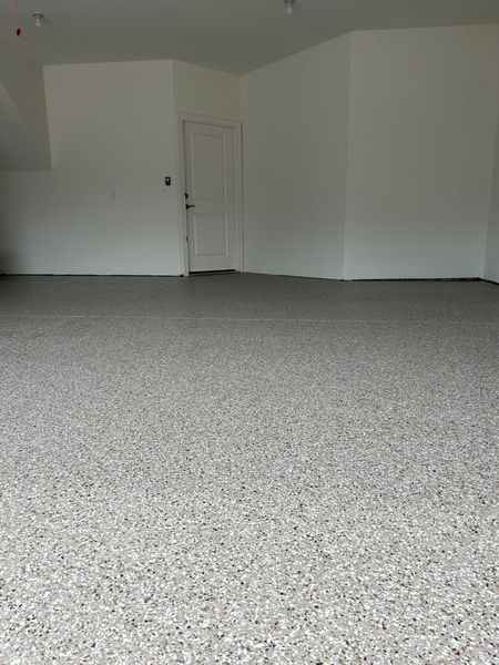An empty garage with a speckled gray floor and white walls. A white door is visible.