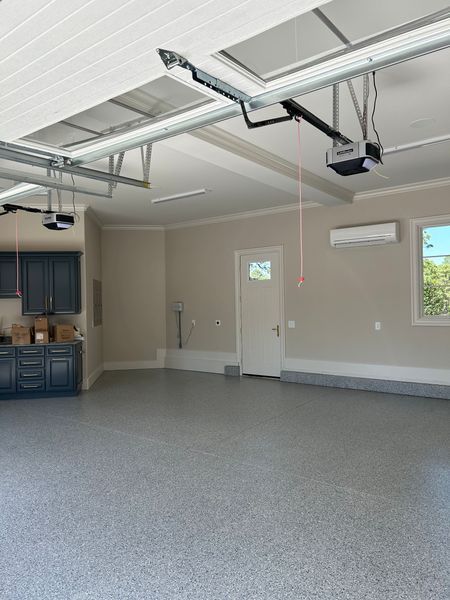 Spacious garage with gray epoxy floor, cabinets, white door, and overhead garage door openers.