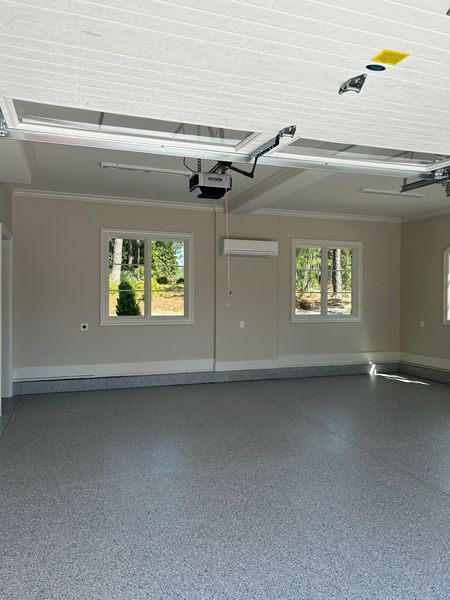 Empty garage interior with gray speckled floor, white trim, two windows, beige walls.