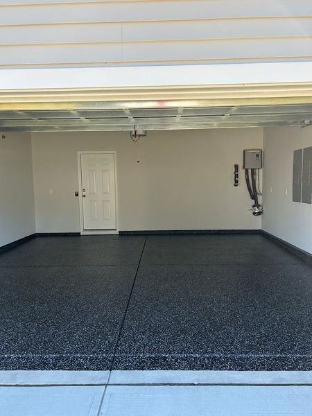 Empty garage with dark speckled floor, light gray walls, and white door.