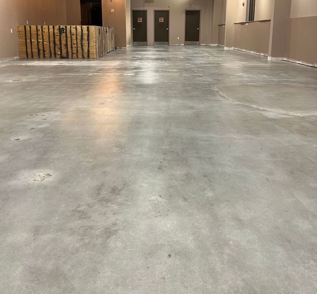 Empty concrete floor of a large room with three doors in the distance.