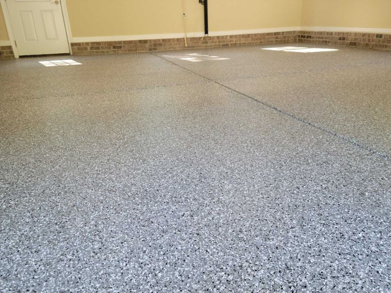 Epoxy-coated garage floor with flecks of gray, white, and black. Walls are beige, with a brick border. A white door is on the left.