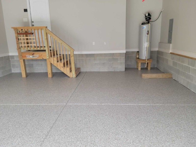 Garage interior with gray speckled floor, stairs, and water heater on a stand.
