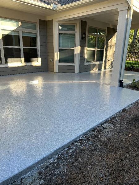 A gray-speckled concrete patio under a covered porch with windows.