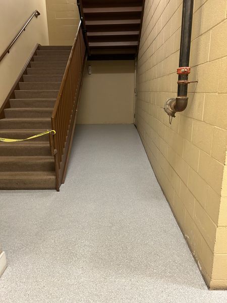 Staircase and ramp in a building. Stairs have a brown handrail. Ramp is light gray. Beige brick wall to the right.