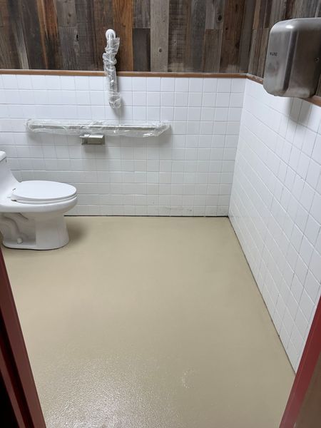 Small public restroom with white tile walls, wood paneling, beige floor, toilet and paper towel dispenser.