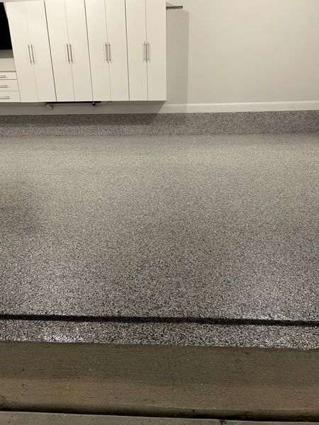 Garage floor with speckled gray epoxy finish and white cabinets on wall.