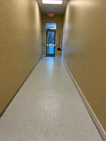 Narrow hallway with beige walls, a speckled gray floor, and a door at the end.