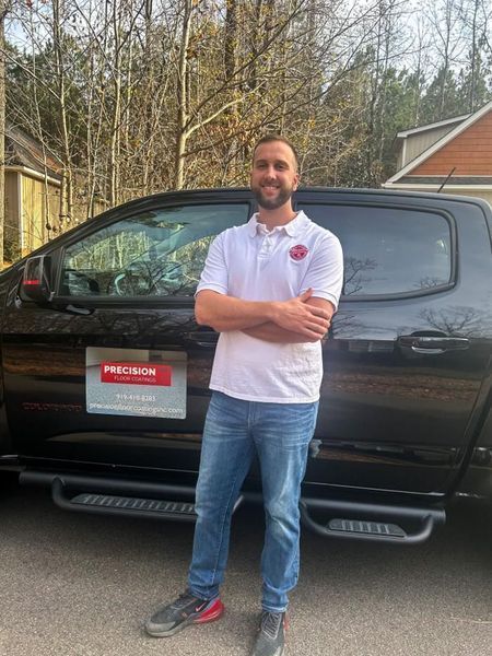 Man in white polo and jeans smiles, arms crossed, beside a black pickup truck with Prednom logo.
