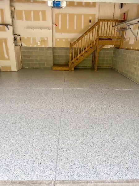 Garage interior with gray speckled epoxy floor, stairs, and exposed cinder block walls.