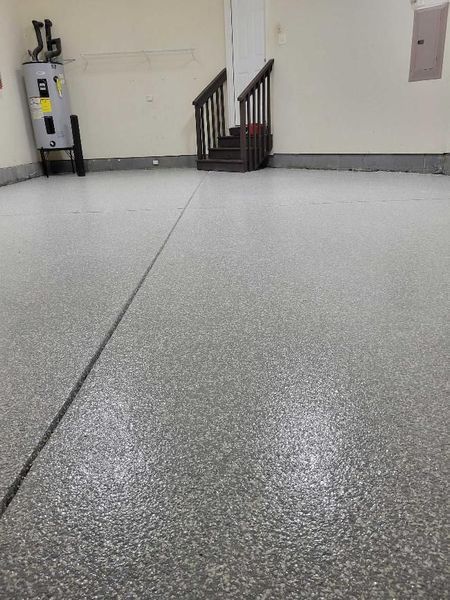 Garage with a speckled gray epoxy floor, water heater, and stairs leading upwards.
