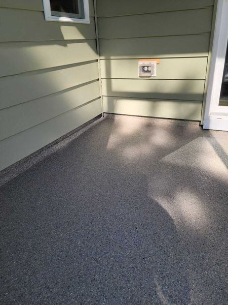 A small, covered porch with a speckled gray floor and pale green siding.